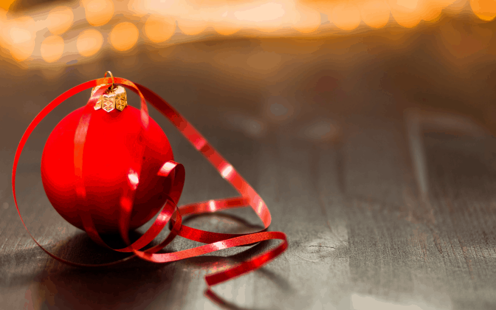 A red Christmas ornament sitting on a brown oakwood table.