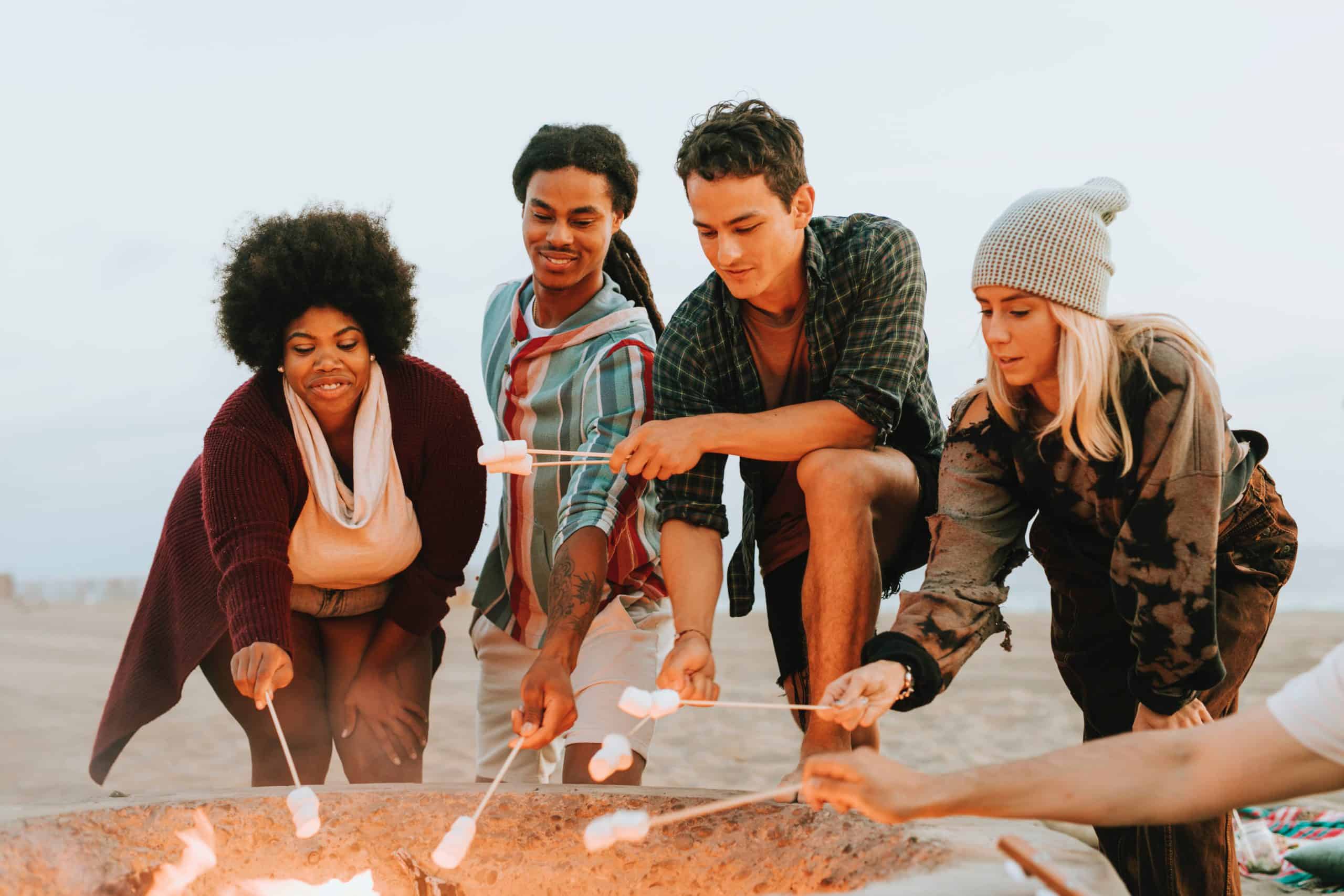 A group of young people toasting marshmallows in a beach bonfire