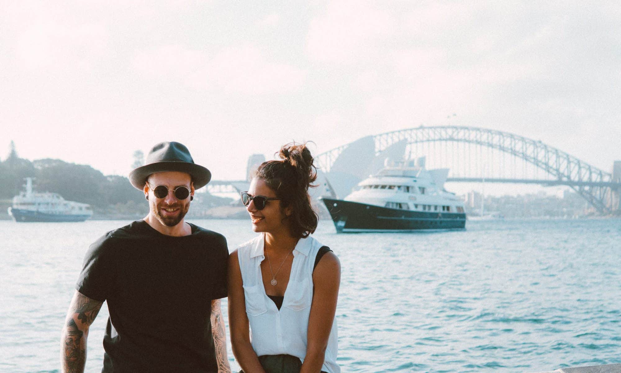 A man and woman holding hands in front of the Sydney Harbour Bridge