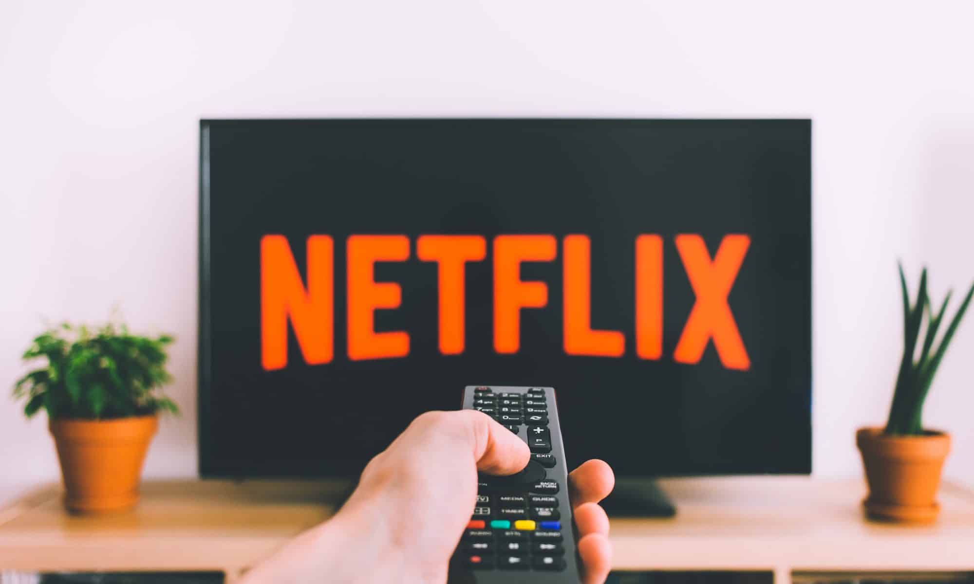 A person pointing a remote control towards the TV that says Netflix on it