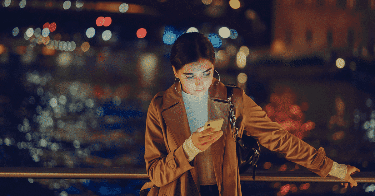 A young woman standing outside at night on her phone with car lights in the background.