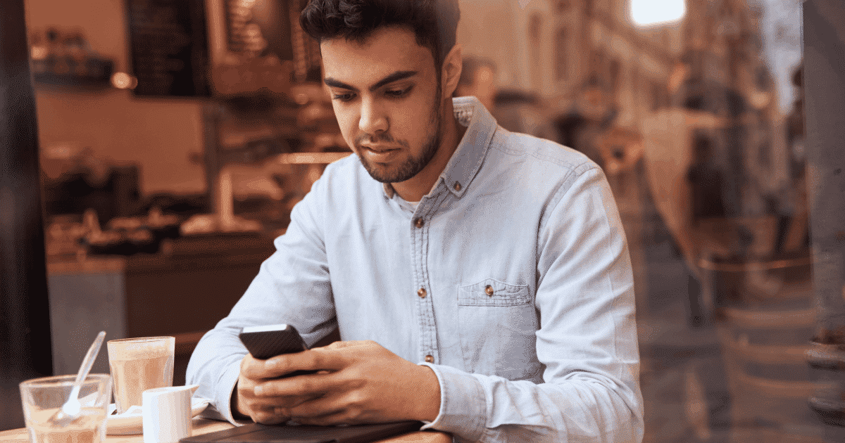 Young man in a buttoned-up shirt on his phone at a cafe